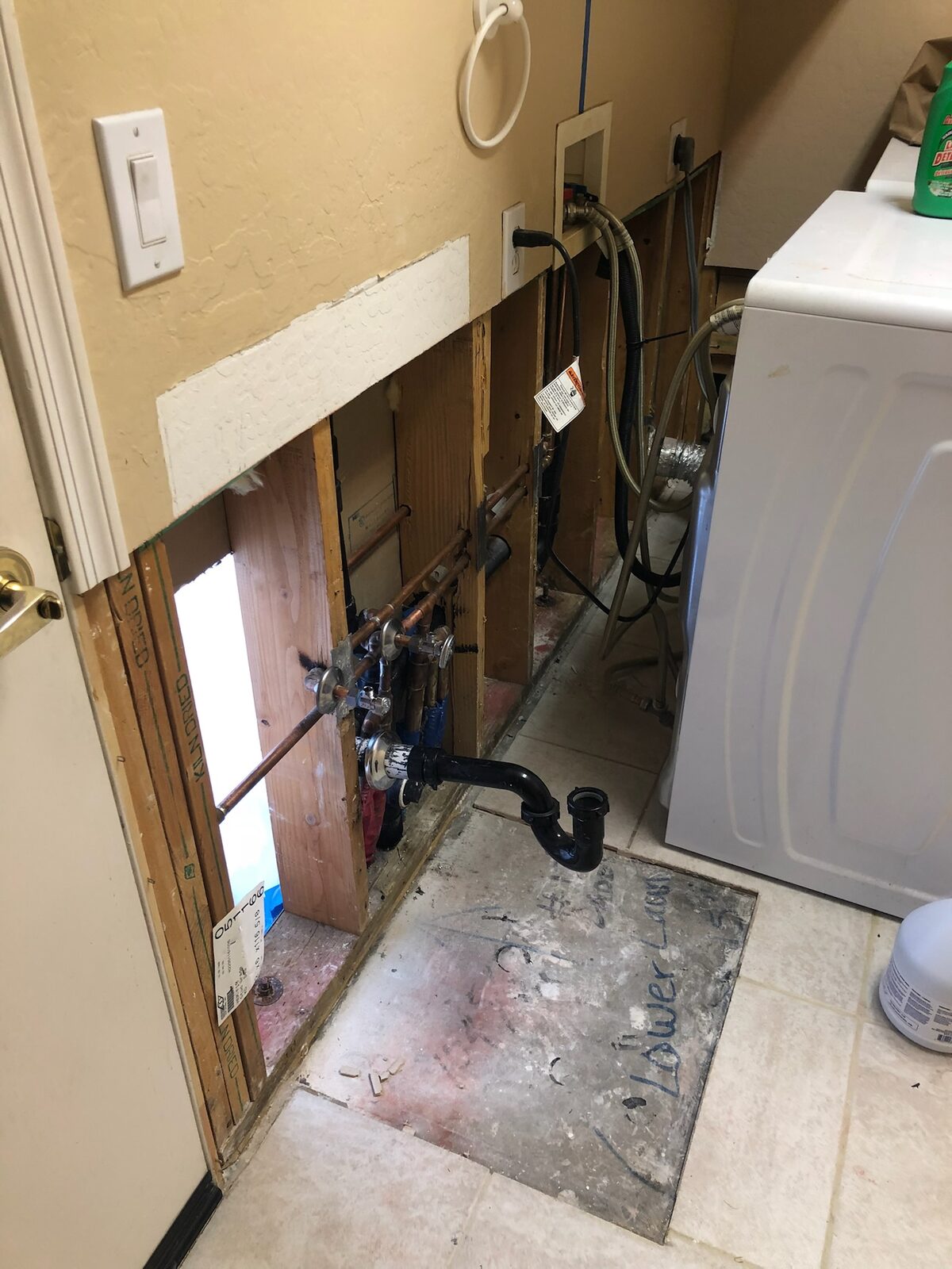Laundry room wall opened to expose supply lines and drain plumbing during drying