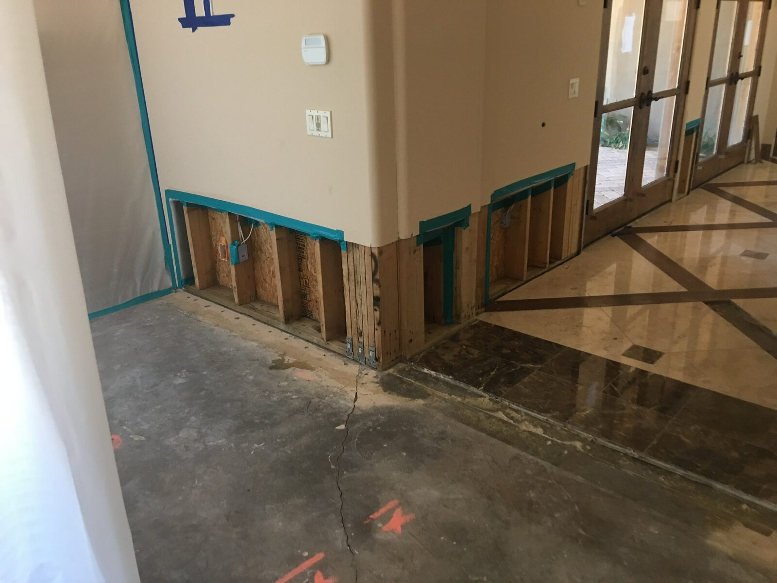 Lower drywall removed to expose framing after water damage beside a marble tile floor