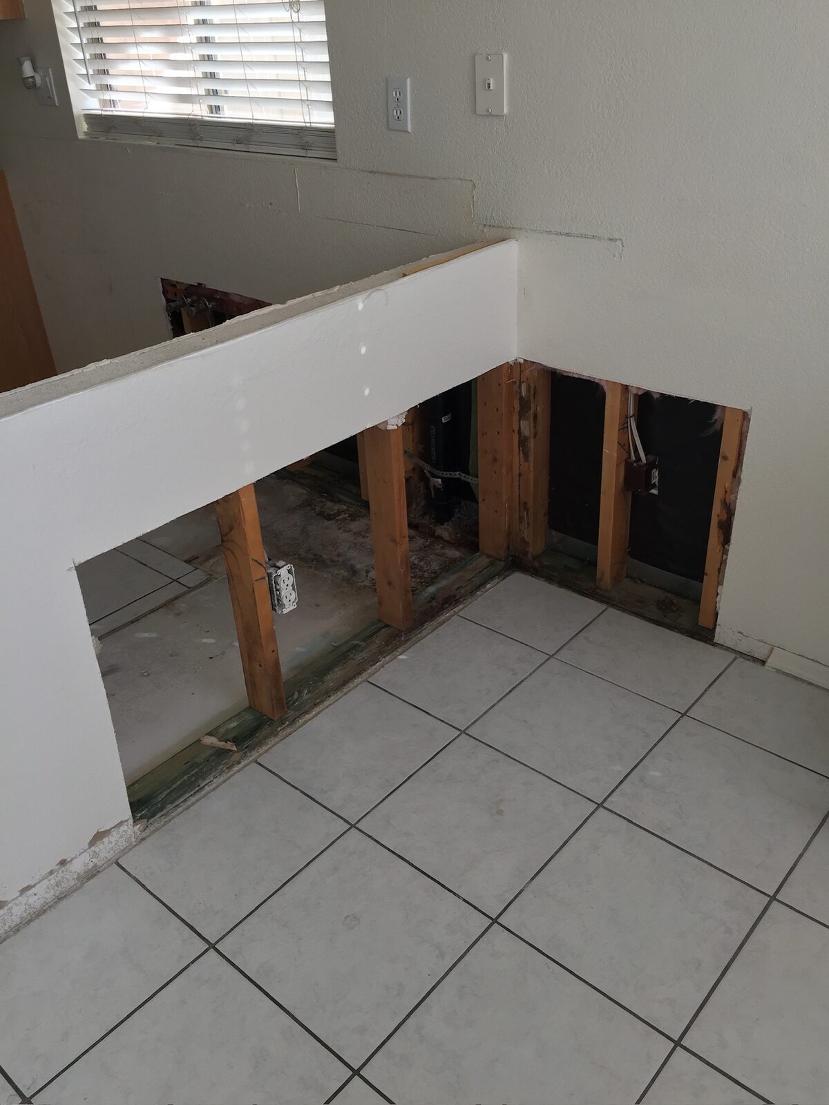 Lower drywall removed from a half wall exposing studs with water staining at the base