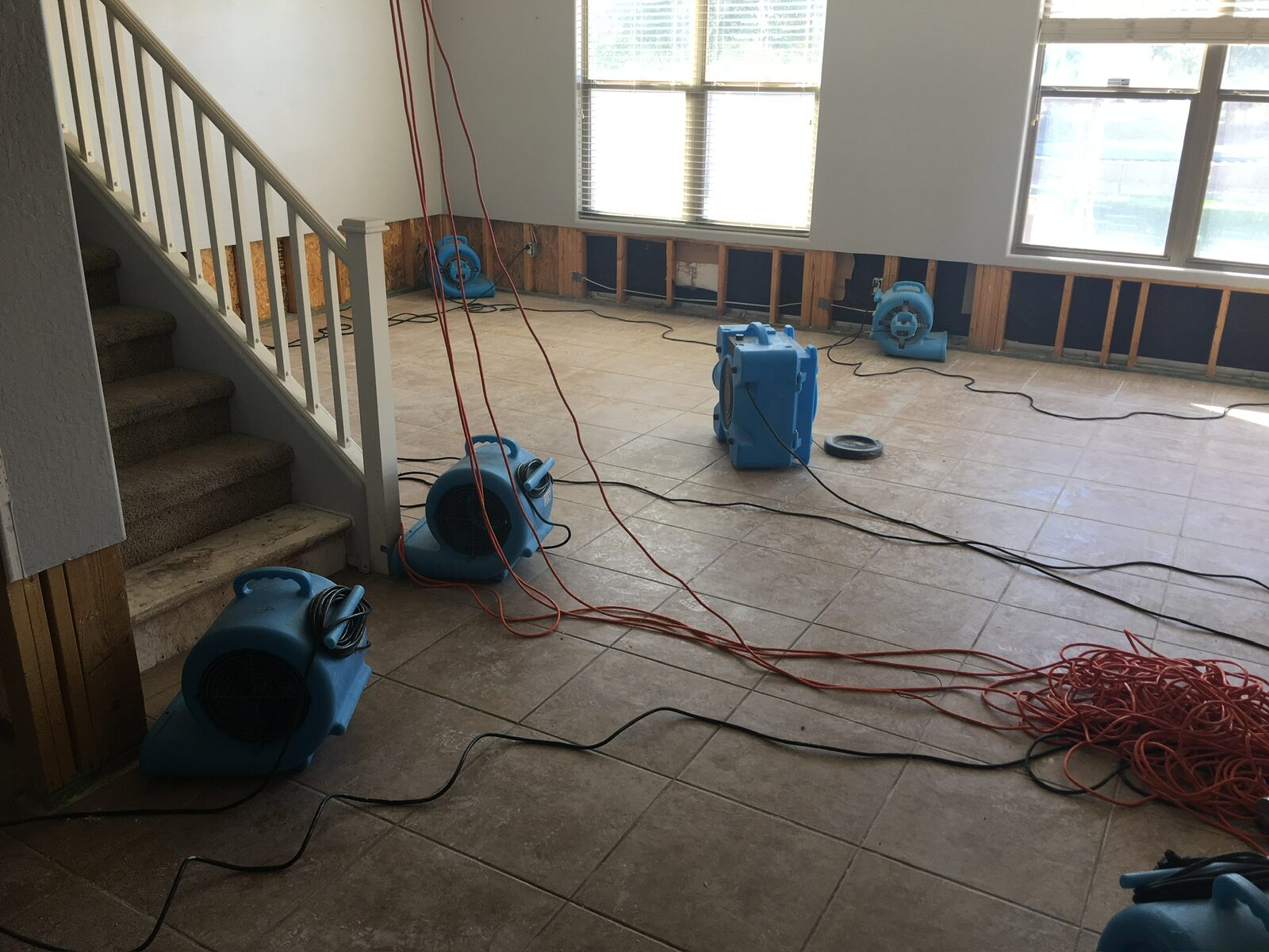 Multiple air movers and a dehumidifier drying a living room with flood cuts along the walls