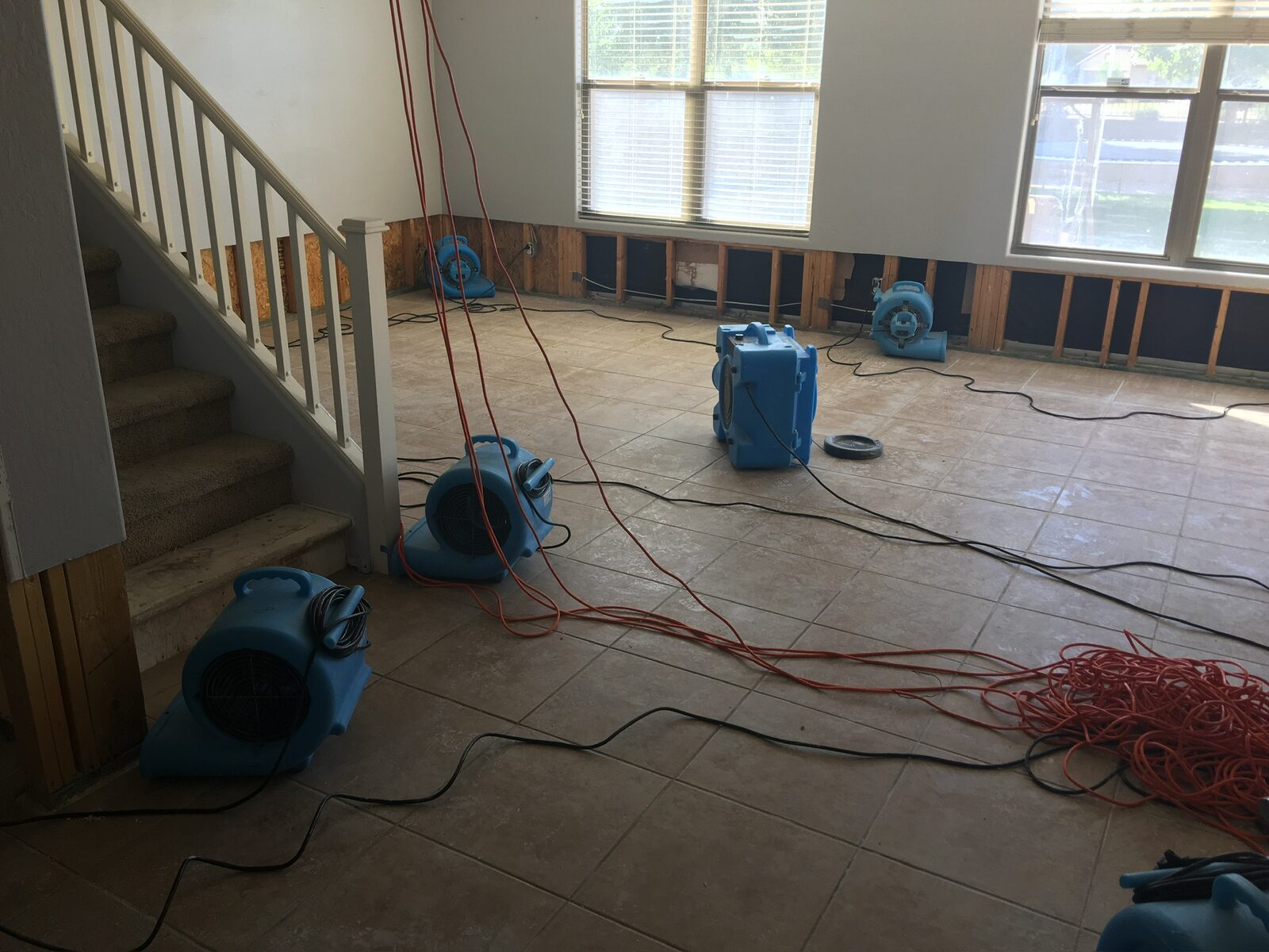 Multiple air movers drying a tiled living area with lower drywall removed