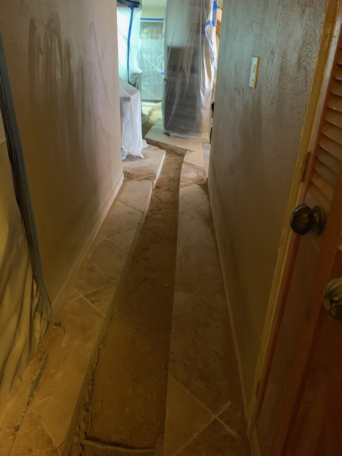 Narrow channel cut through tile floor in a hallway with furniture wrapped in plastic