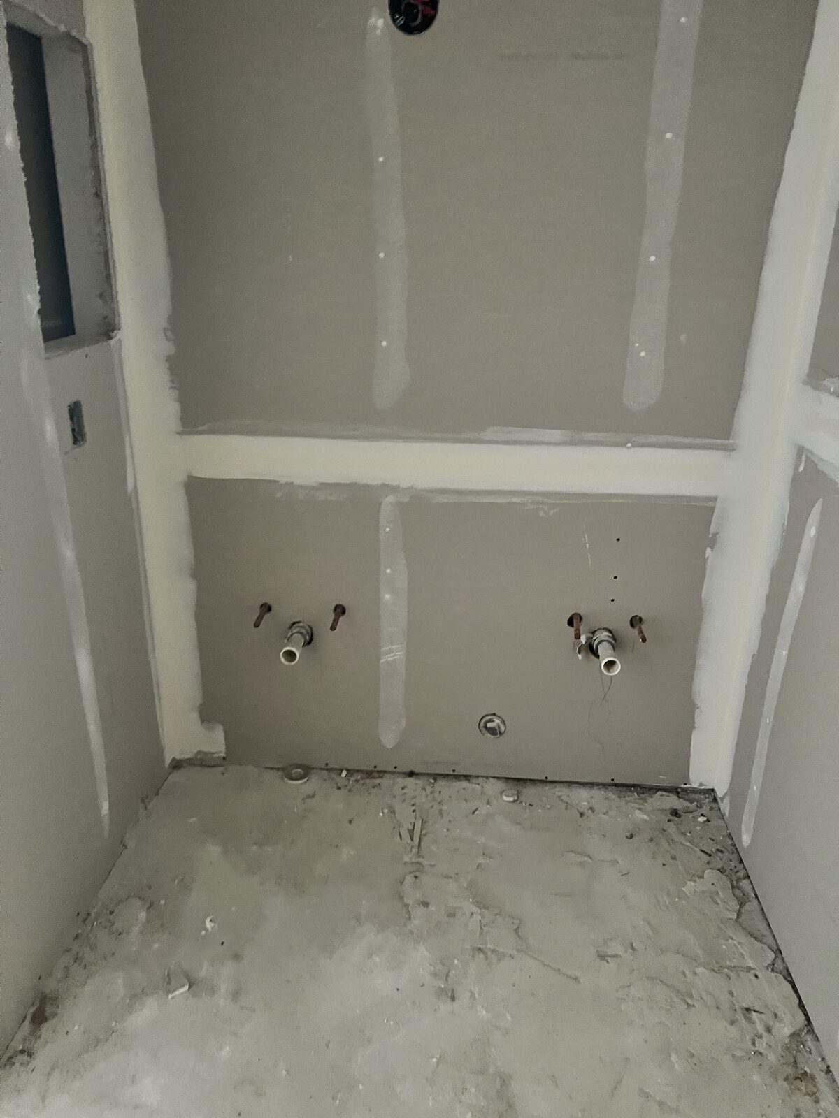 New drywall hung and taped in a laundry alcove with supply lines stubbed out