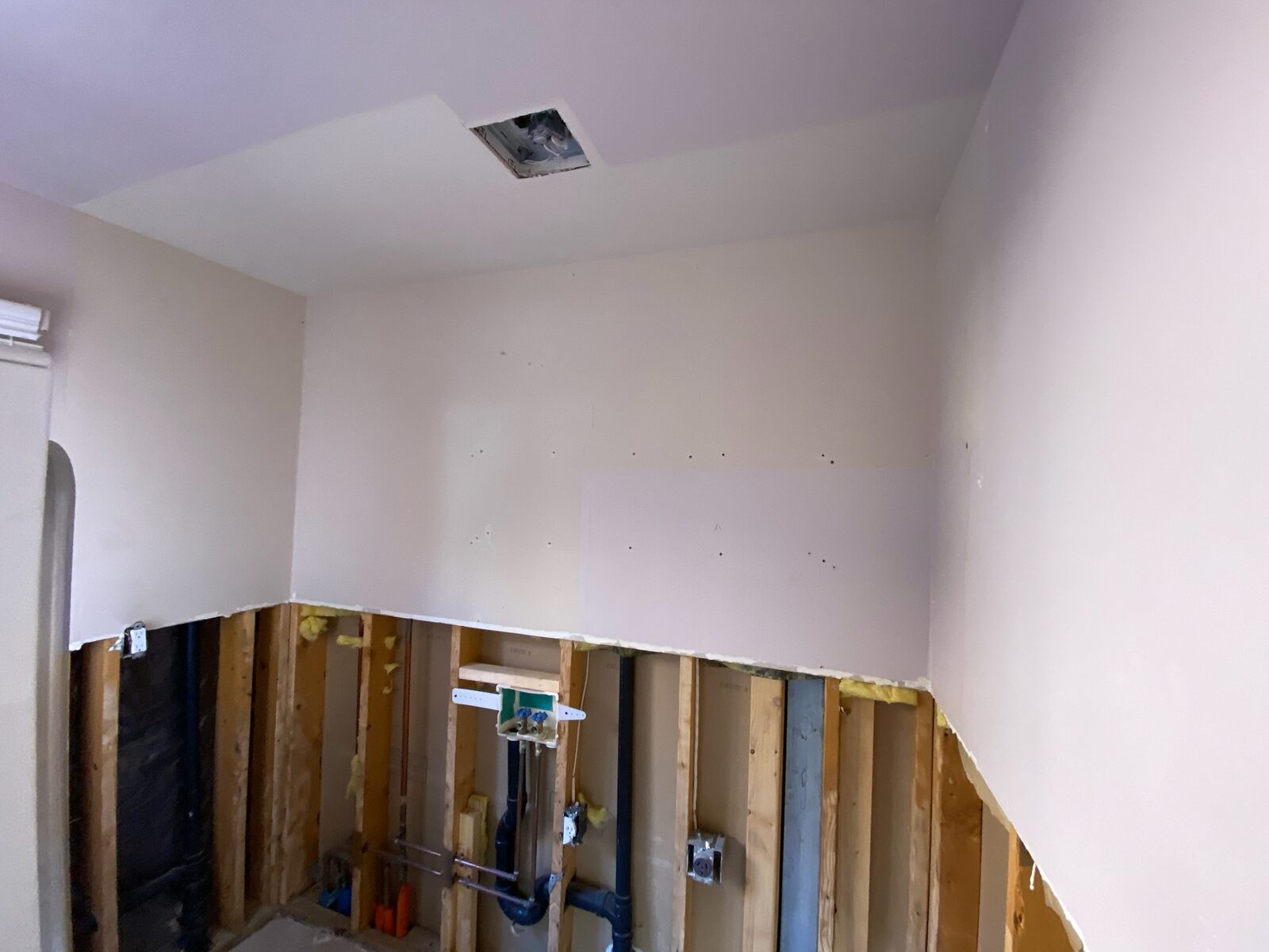 New drywall installed on upper walls with studs and supply plumbing still exposed below