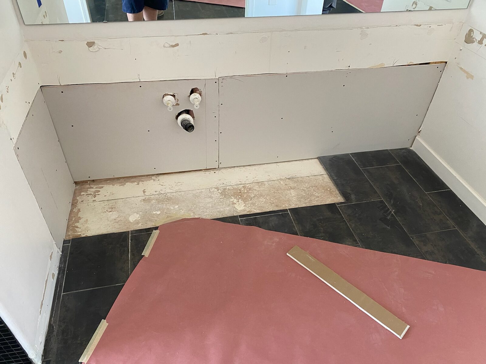 New drywall panels installed behind a removed bathroom vanity with plumbing stub outs visible
