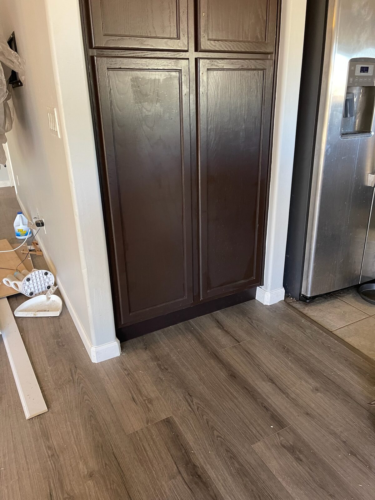 New wood-look plank flooring installed at a pantry with dark cabinet doors and new baseboard