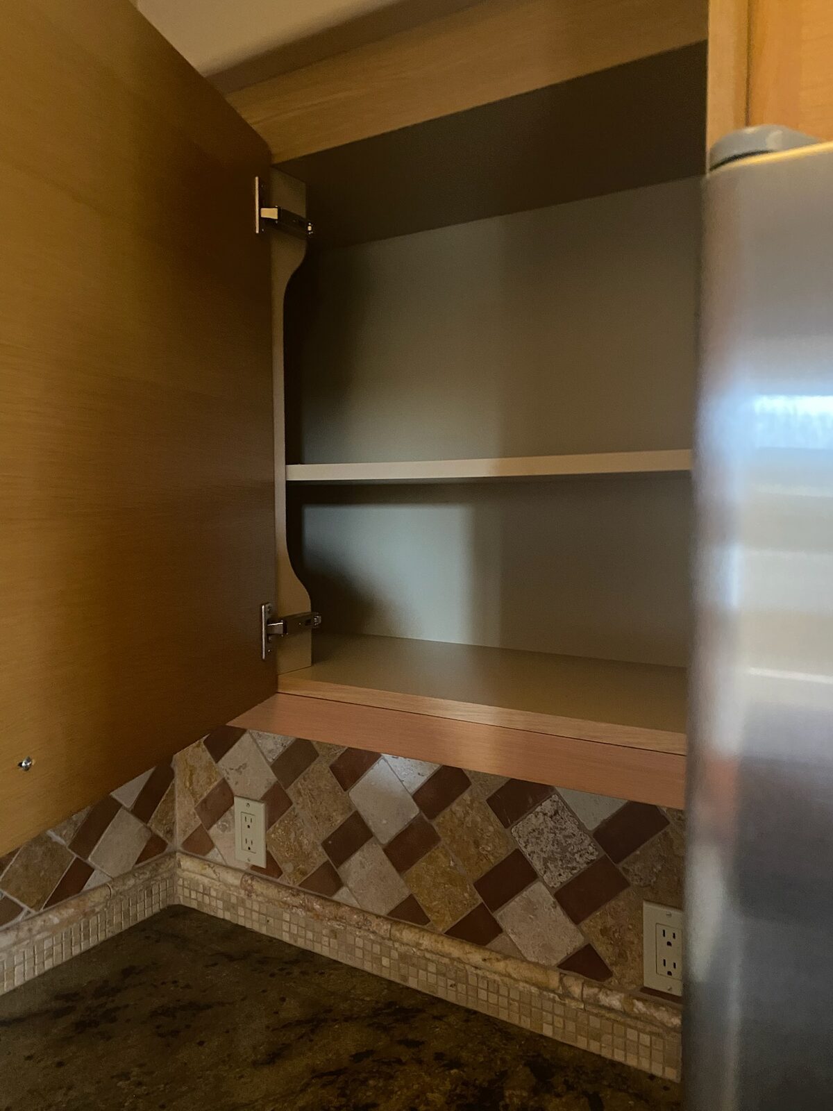 Open upper cabinet interior above a granite counter and tumbled stone backsplash