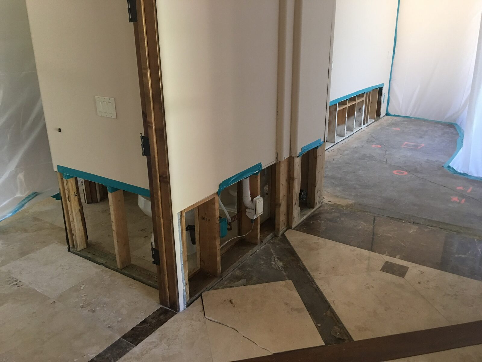 Partition walls with lower drywall removed and taped edges beside a slab marked for trenching