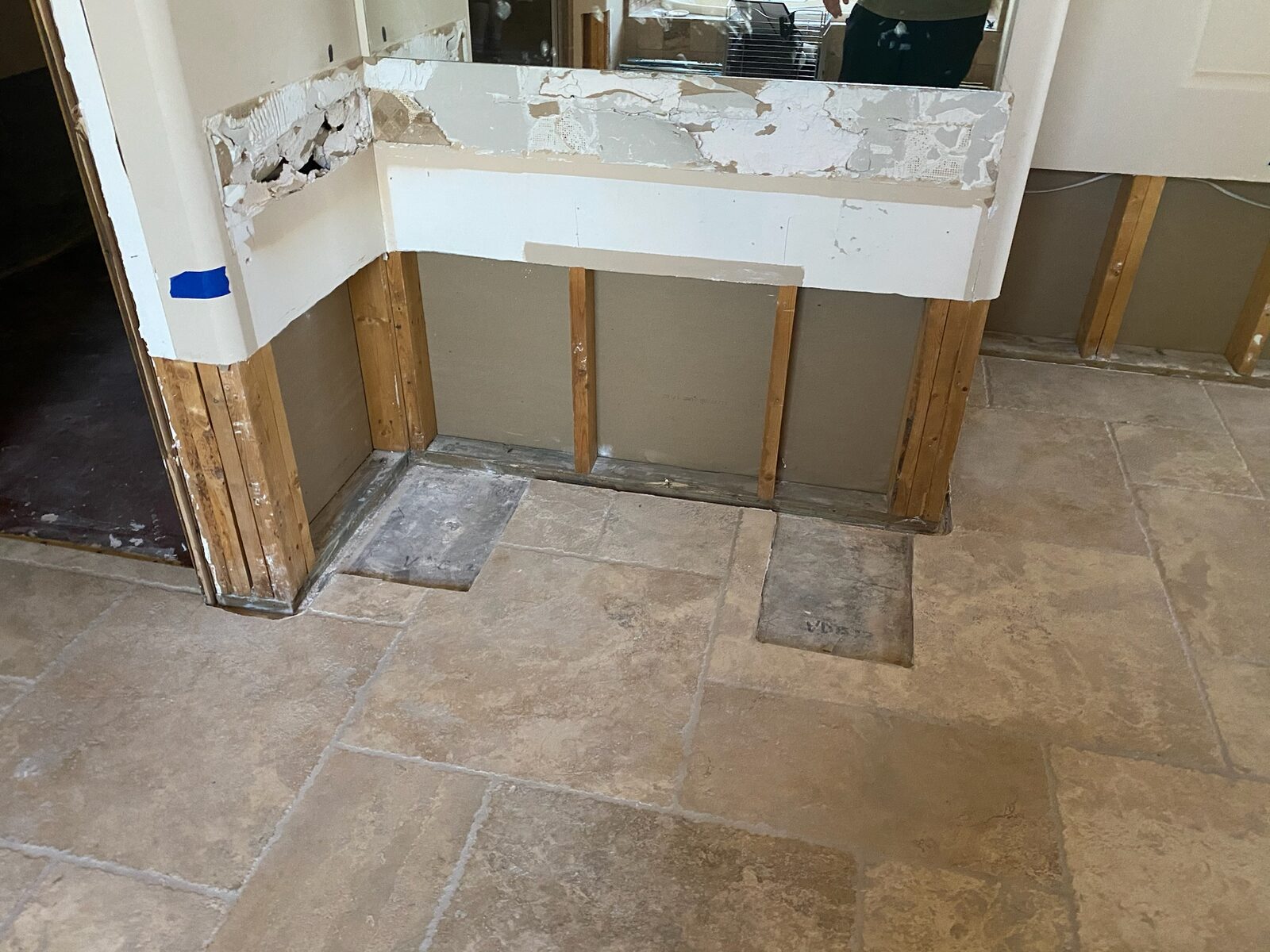 Pony wall stripped to studs beside a mirror in a room with travertine tile flooring