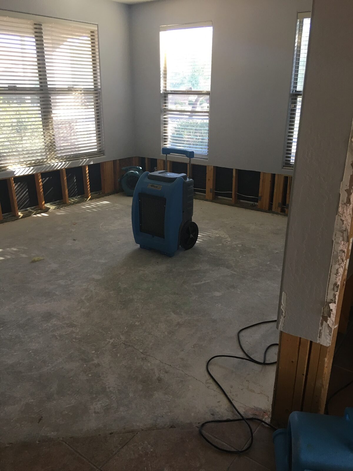 Portable dehumidifier and air movers drying a room with flood-cut walls and bare concrete floor