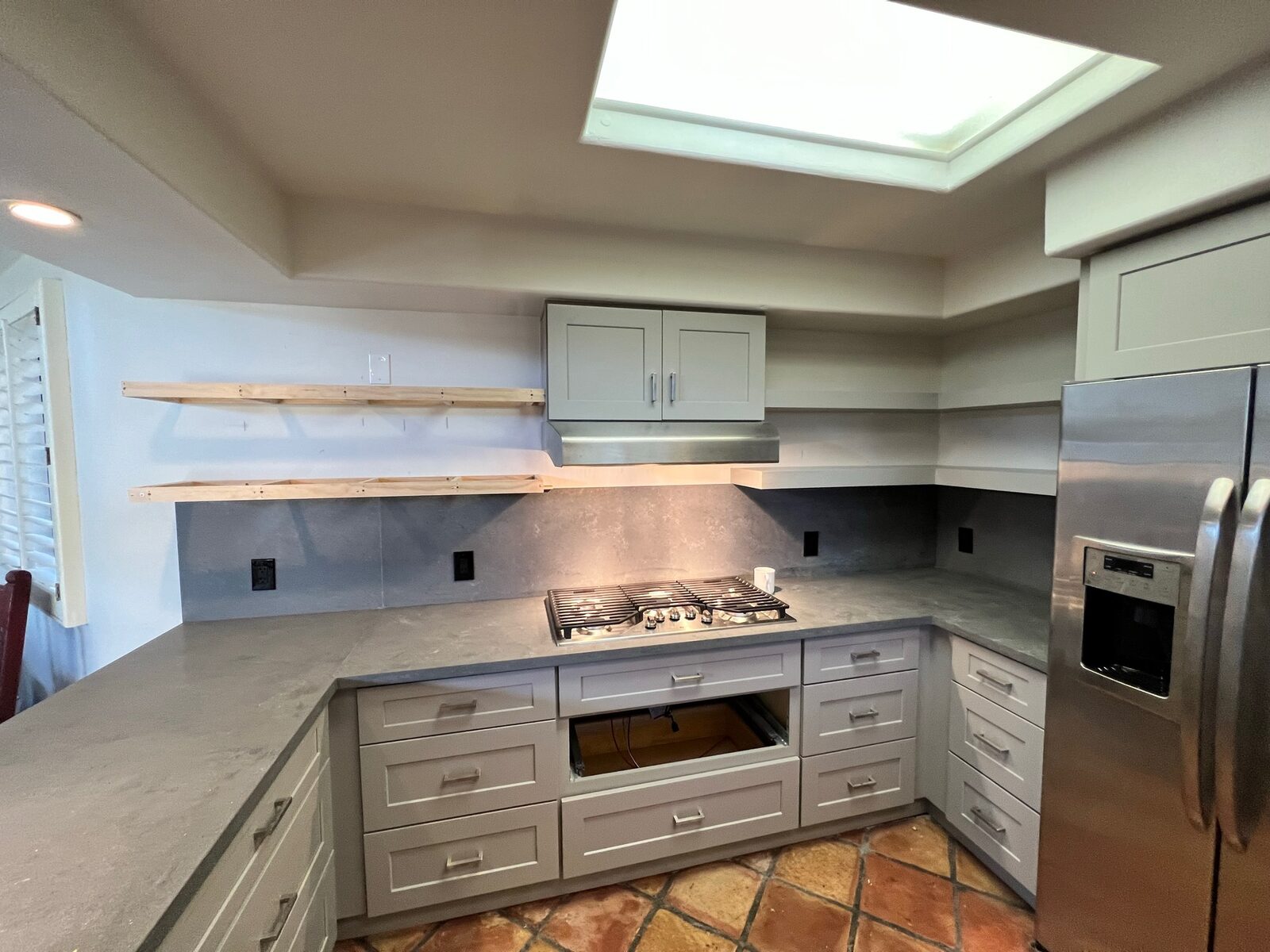 Remodeled kitchen with gray shaker cabinets, gas cooktop, concrete-look countertops and open shelf framing