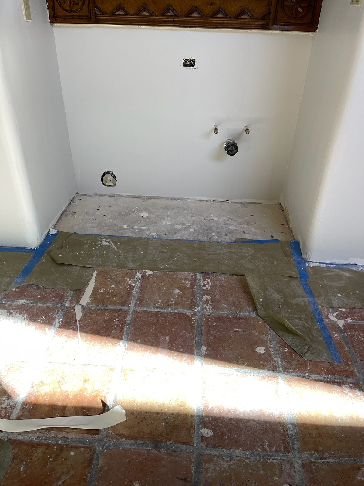 Repainted laundry alcove with new supply valve box above a saltillo tile floor