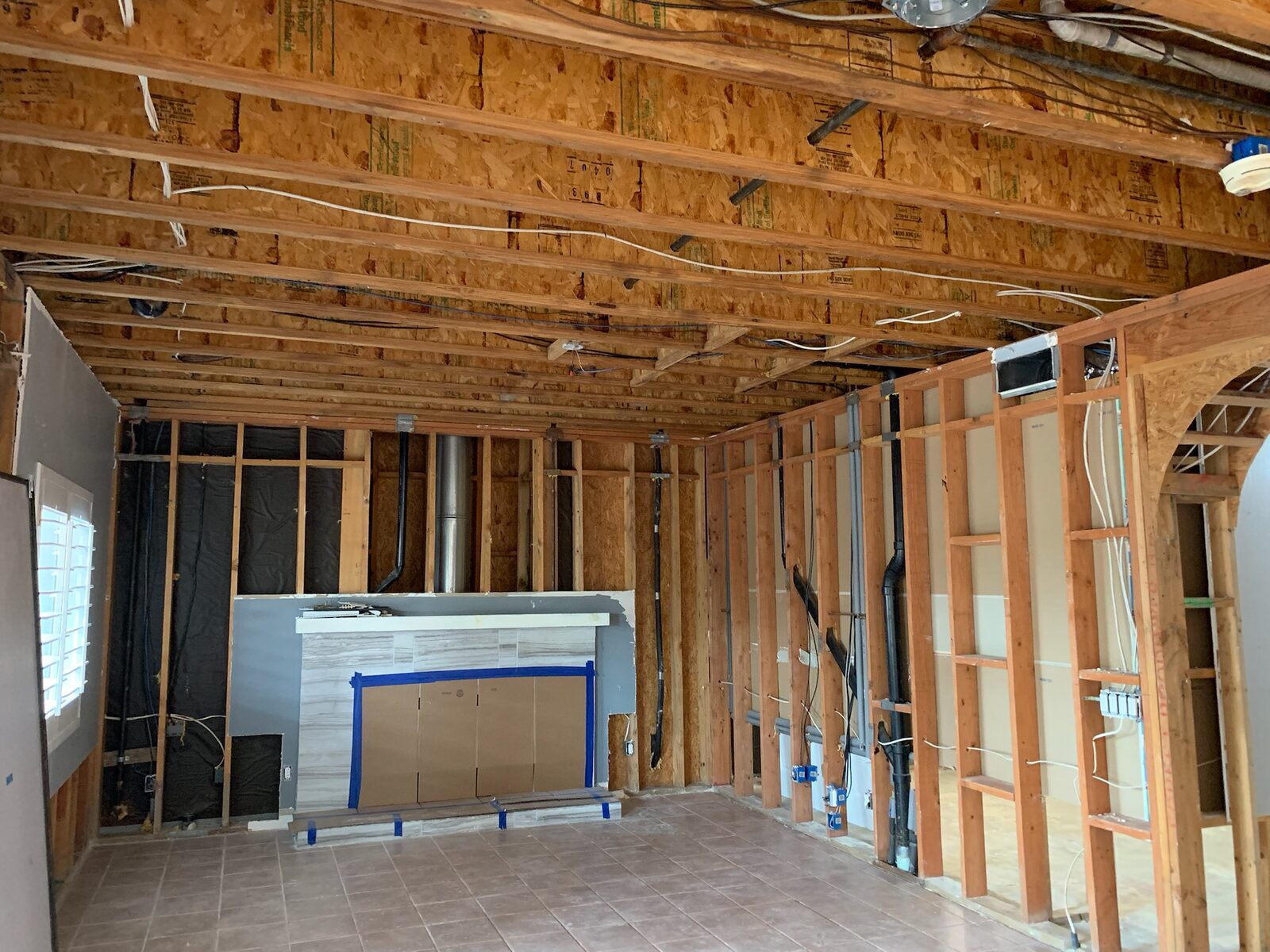 Room stripped to framing with ceiling joists exposed and a fireplace protected by cardboard