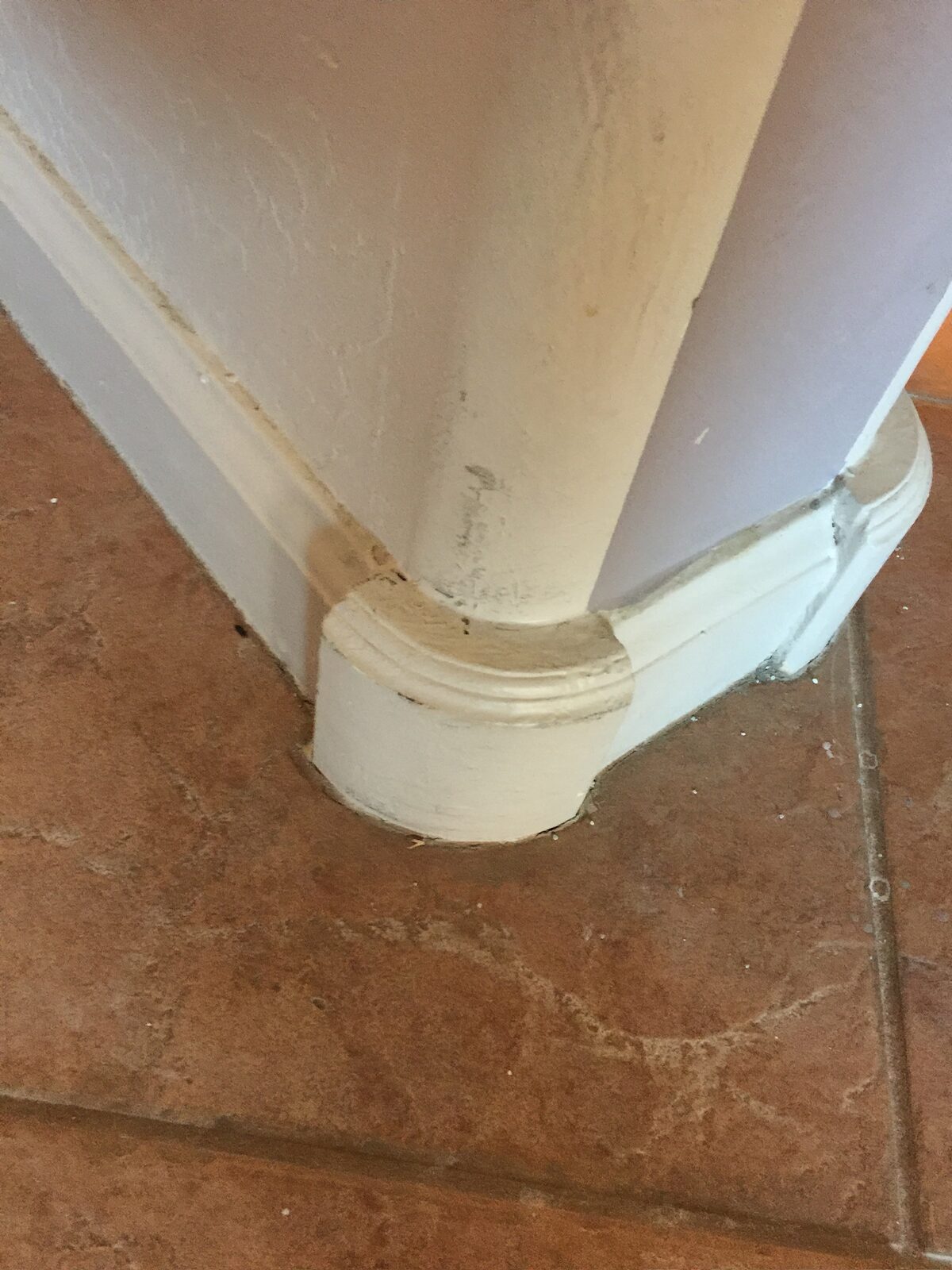 Rounded baseboard corner with patched trim awaiting paint above brown tile flooring