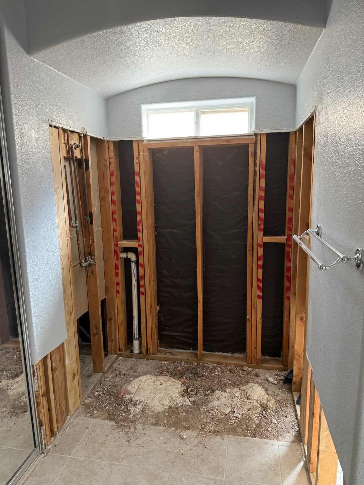 Shower area stripped to wood framing and moisture barrier below an arched ceiling