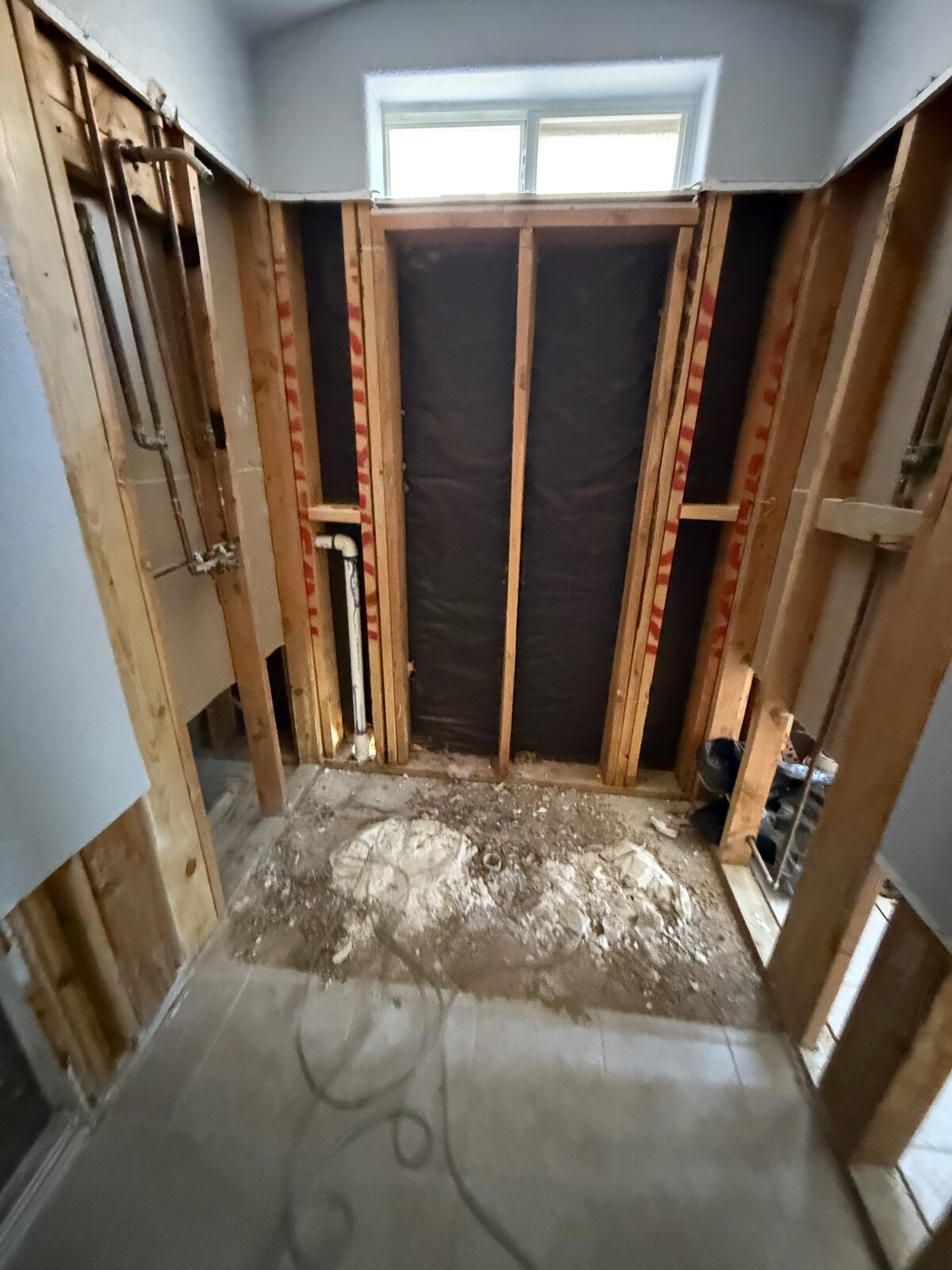 Shower enclosure stripped to studs with black moisture barrier during bathroom demolition