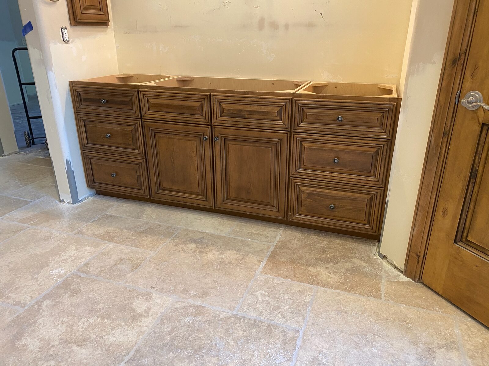 Stained alder vanity base cabinets installed against a wall over travertine tile flooring