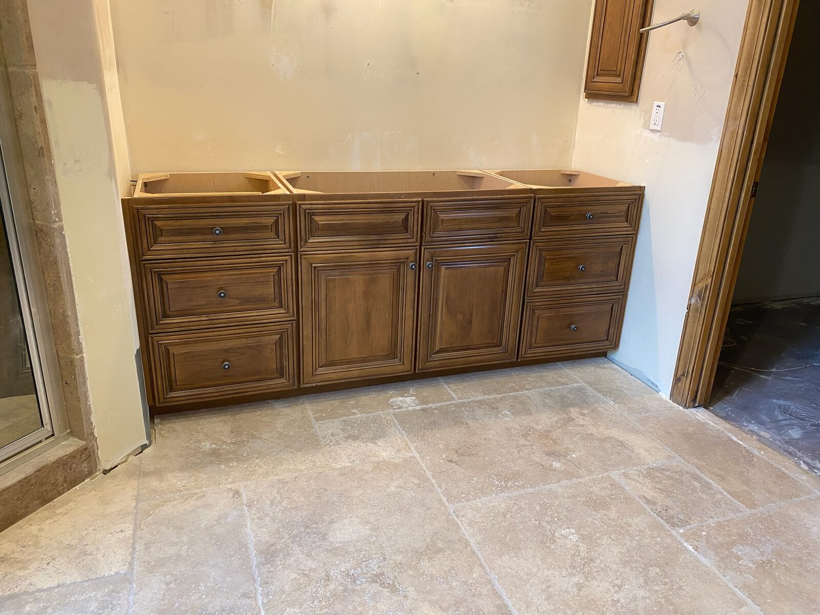 Stained wood vanity cabinets installed on a travertine tile floor