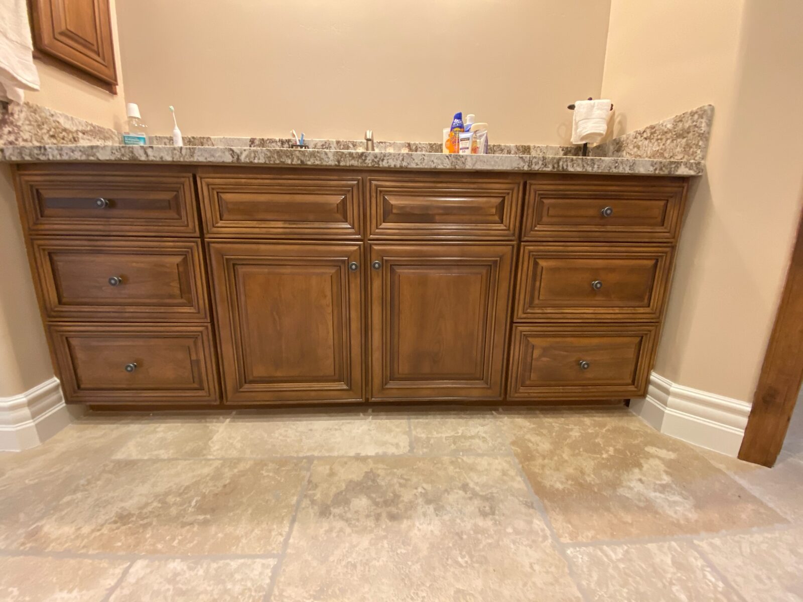 Stained wood vanity with granite countertop and travertine tile floor in a finished bathroom