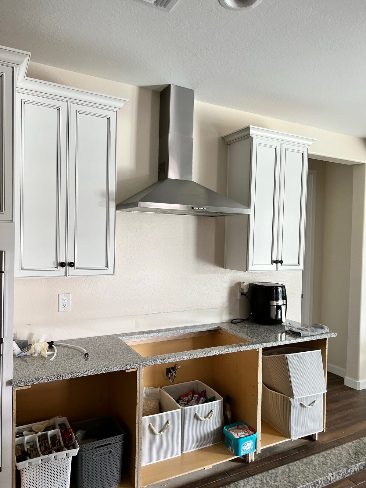 Stainless range hood and white upper cabinets above a granite countertop during a kitchen remodel