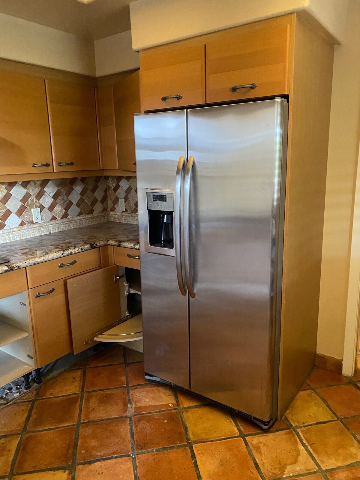 Stainless refrigerator and wood cabinets with doors removed during kitchen repairs