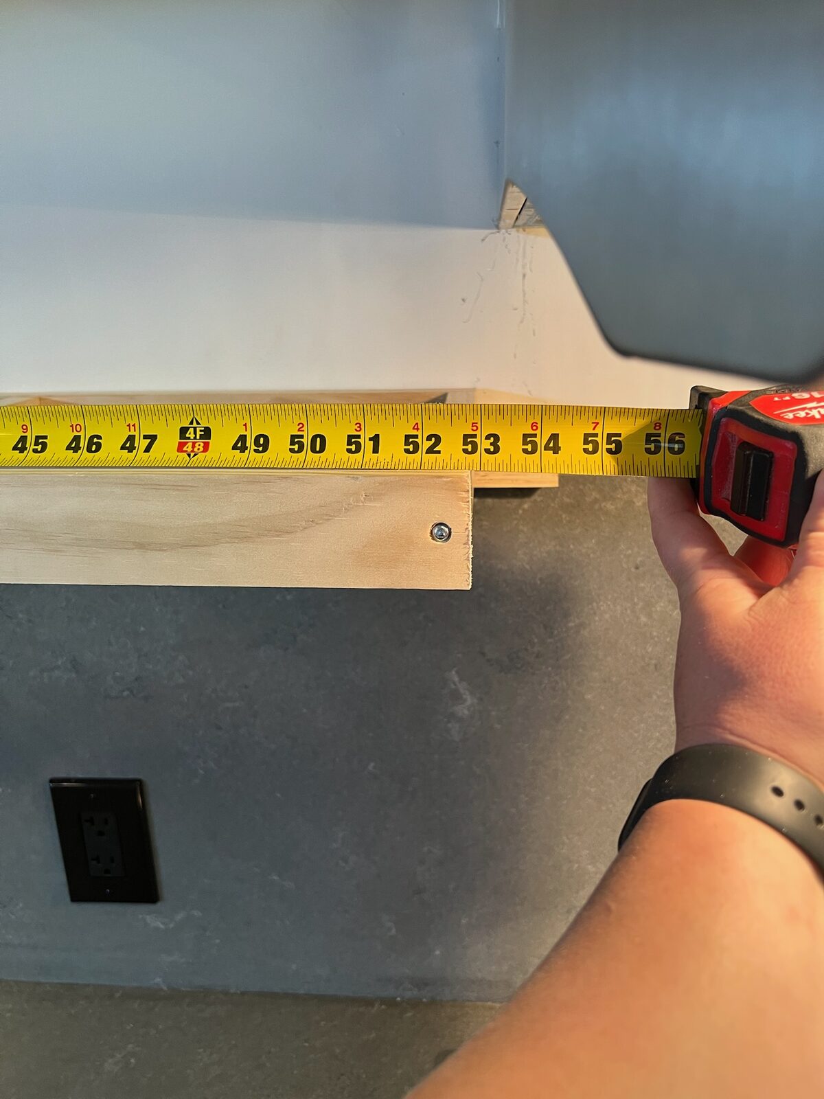 Tape measure extended along a wood shelf cleat above a stone backsplash