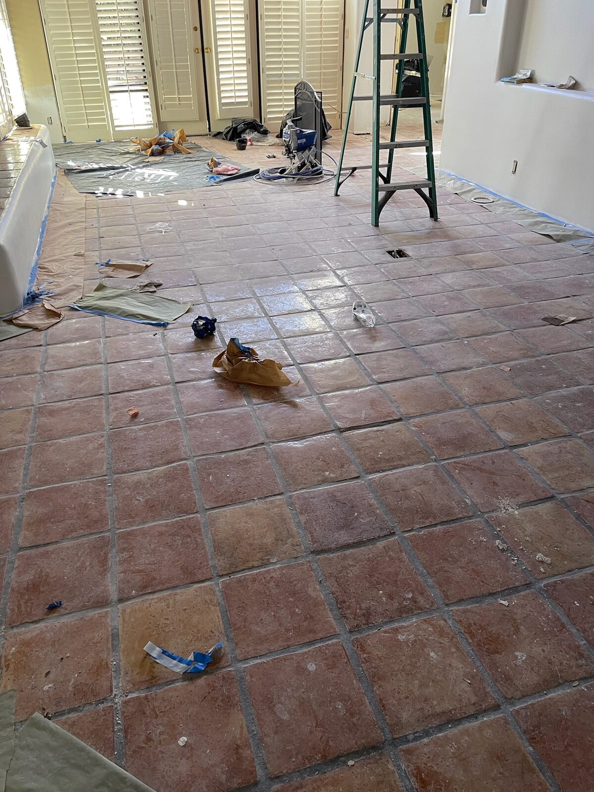 Terracotta tile floor cleaned for refinishing with ladder and paint sprayer staged