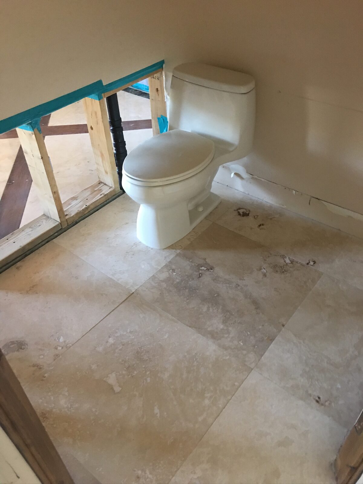 Toilet set on travertine tile beside a partition wall opened to the studs