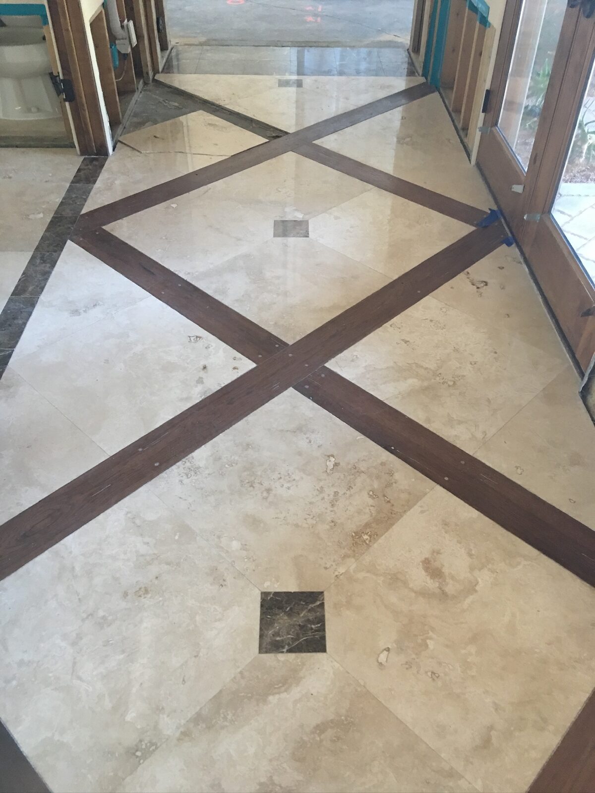 Travertine tile floor with dark wood inlay strips in a diamond pattern near an entry door