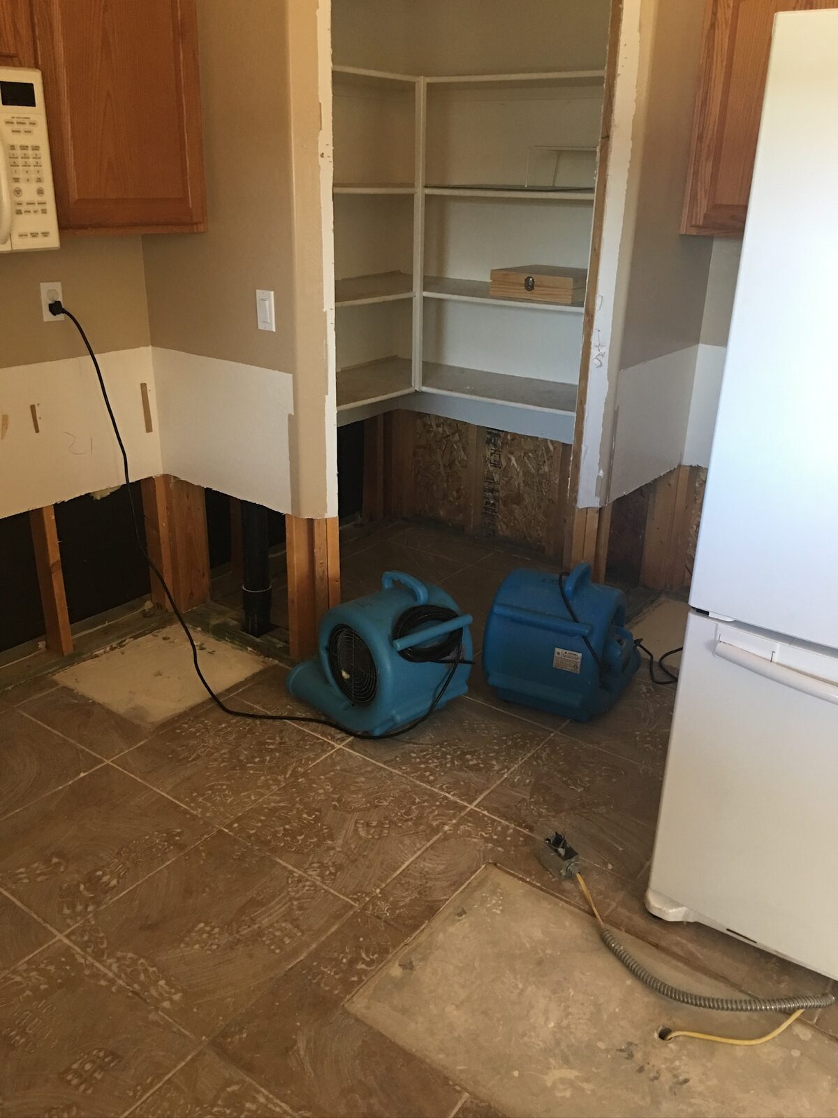 Two air movers drying a kitchen pantry corner with lower drywall removed