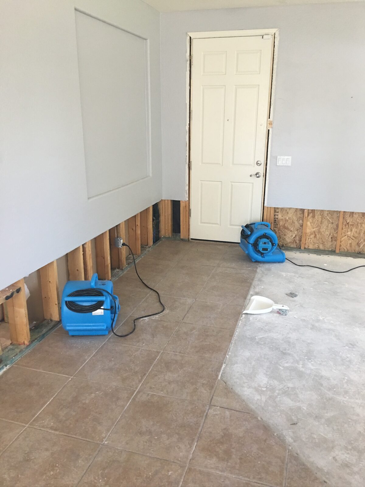 Two air movers drying a room with baseboard drywall removed and tile transitioning to bare concrete