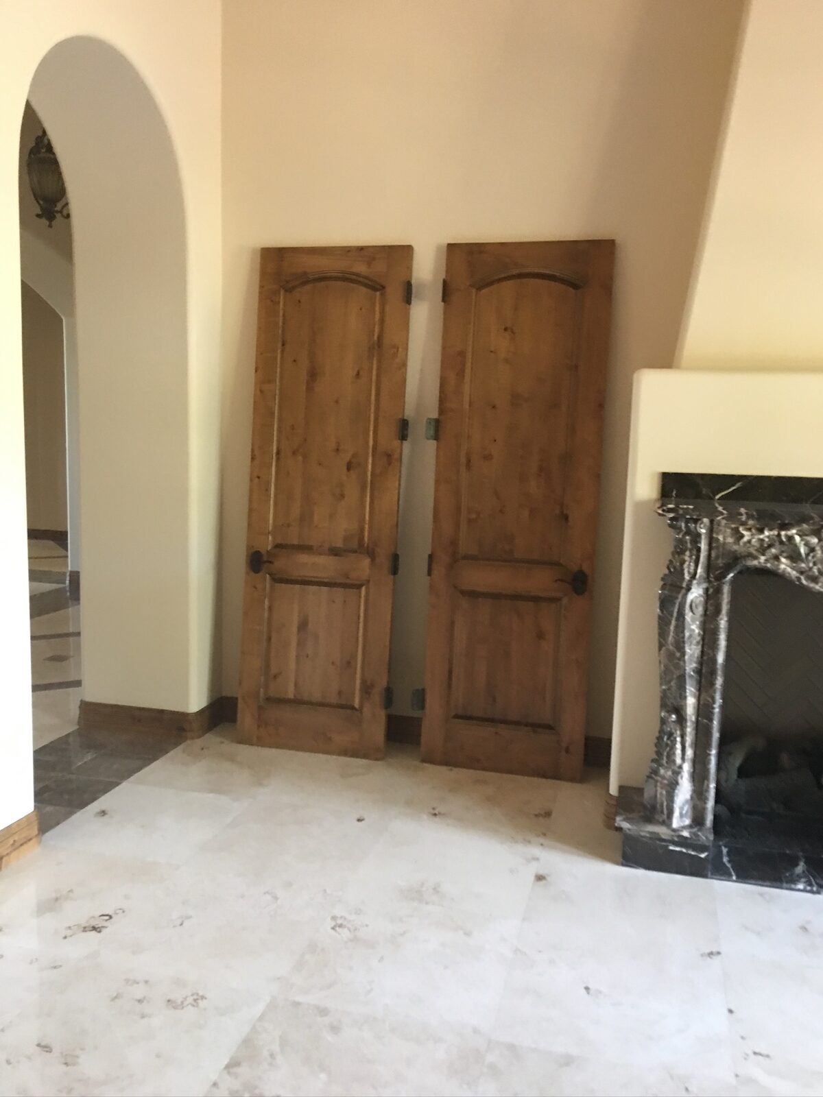 Two arched knotty alder doors staged beside a carved stone fireplace on travertine flooring