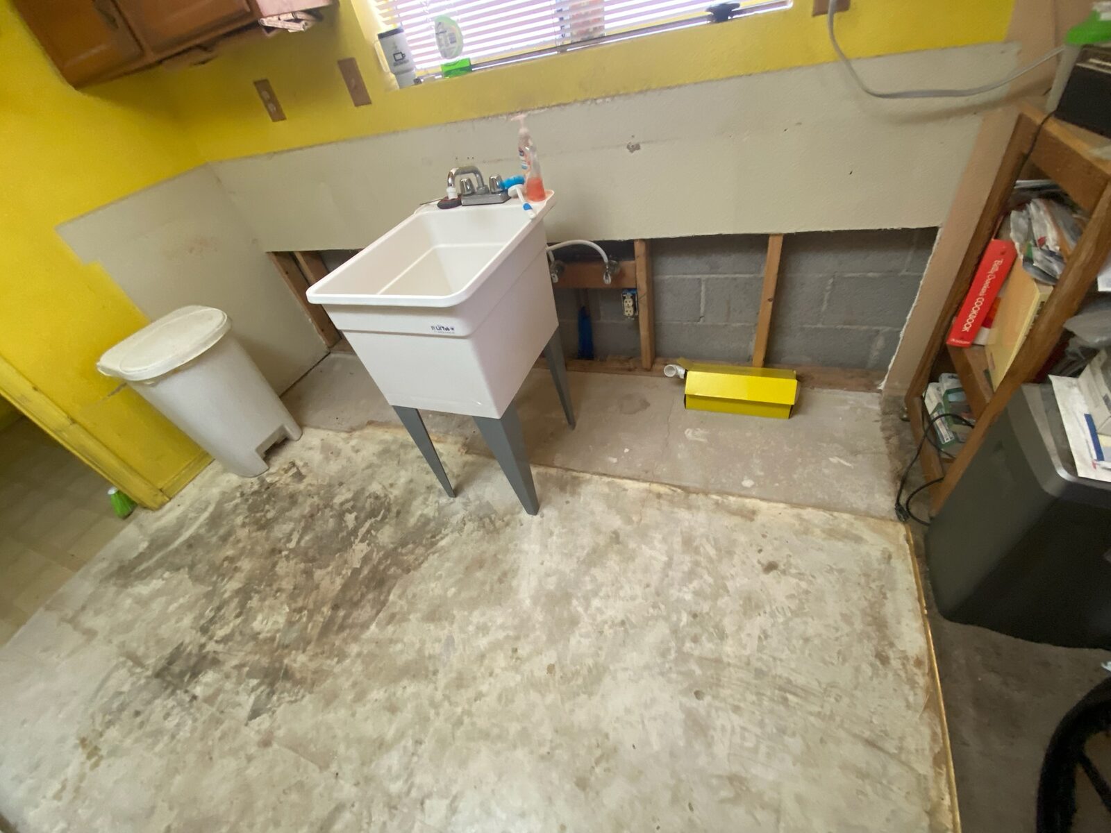 Utility sink on a bare concrete floor with lower drywall removed exposing a block wall