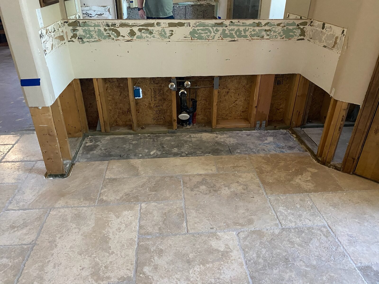 Vanity removed exposing wall framing and rough plumbing below a wall mirror