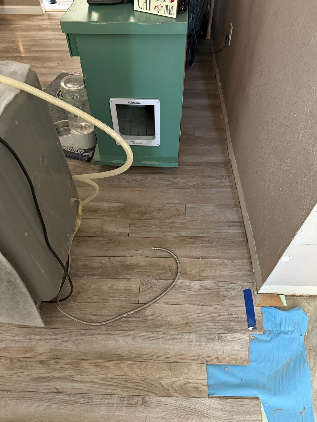 Vinyl plank flooring partially removed exposing blue underlayment along a hallway wall