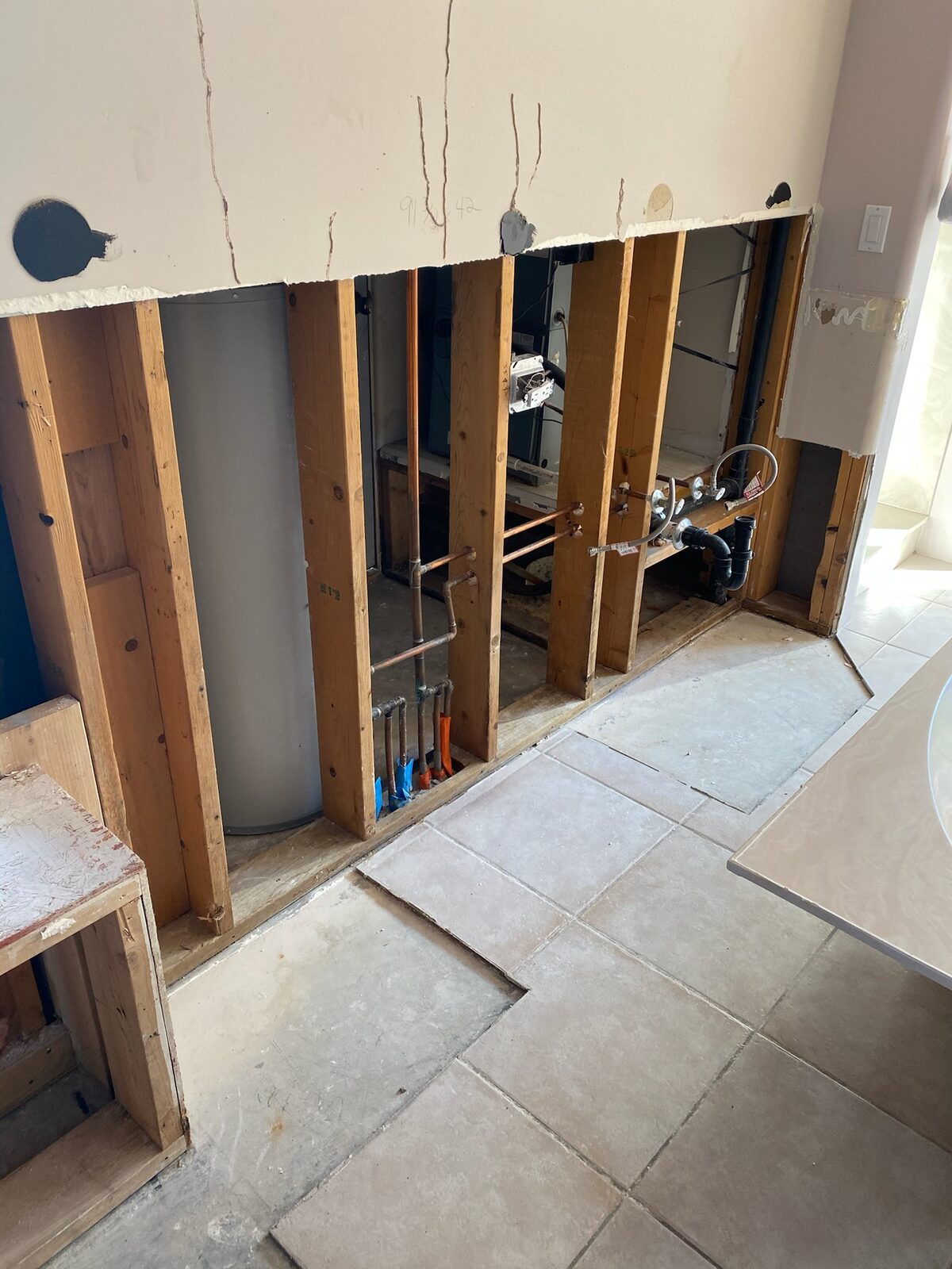 Wall opened to studs showing a water heater and copper supply lines during repairs