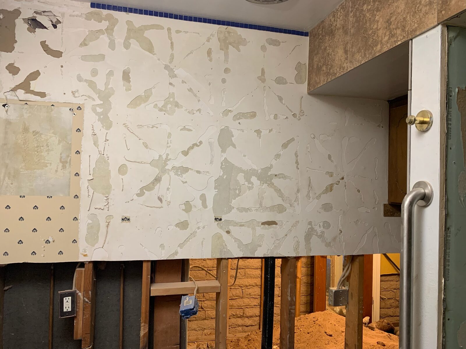 Wall showing adhesive residue after tile removal above exposed stud framing
