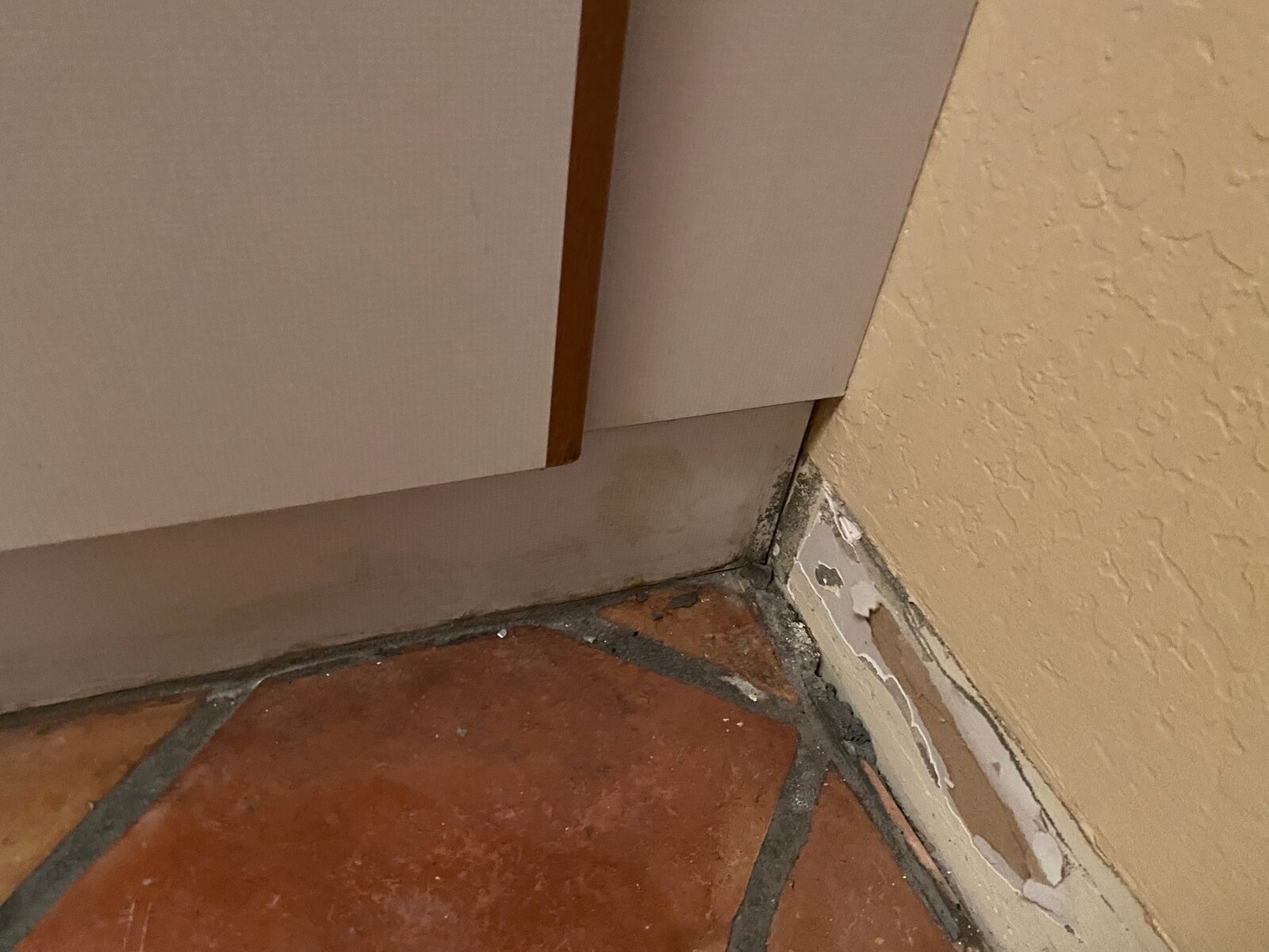 Water staining at the base of a cabinet and baseboard beside terracotta tile flooring