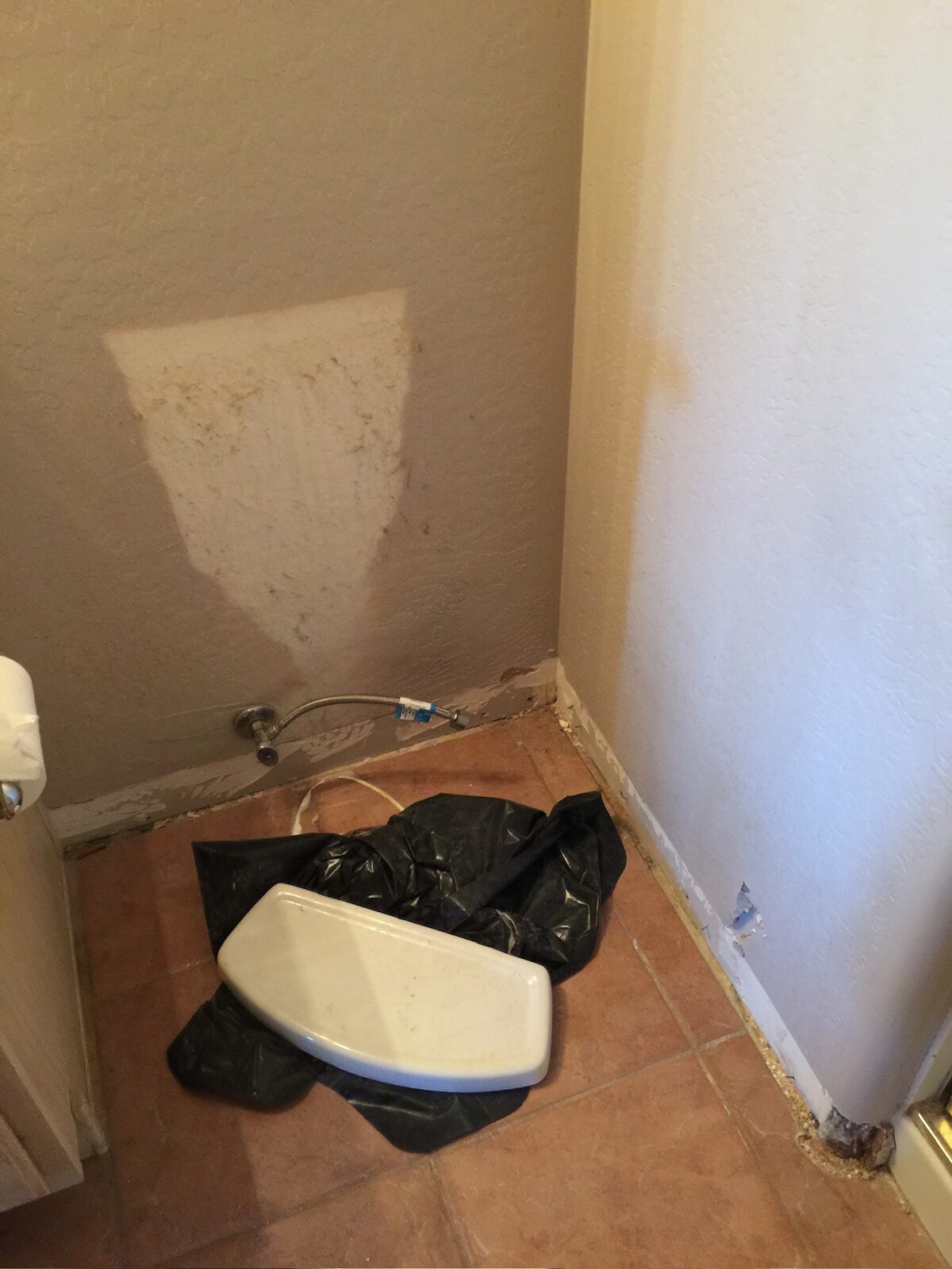 Water staining on a wall corner behind a removed toilet with the supply line disconnected