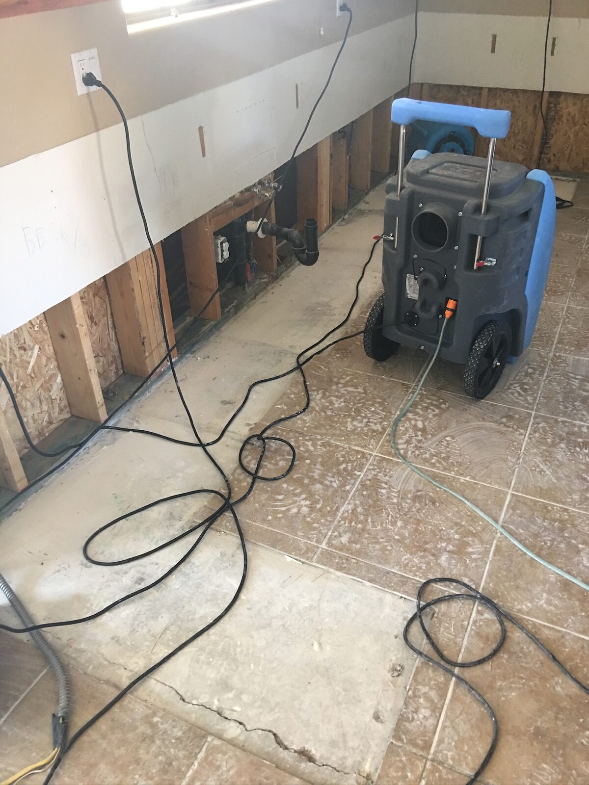 Wheeled dehumidifier drying a kitchen with base cabinets removed and plumbing exposed