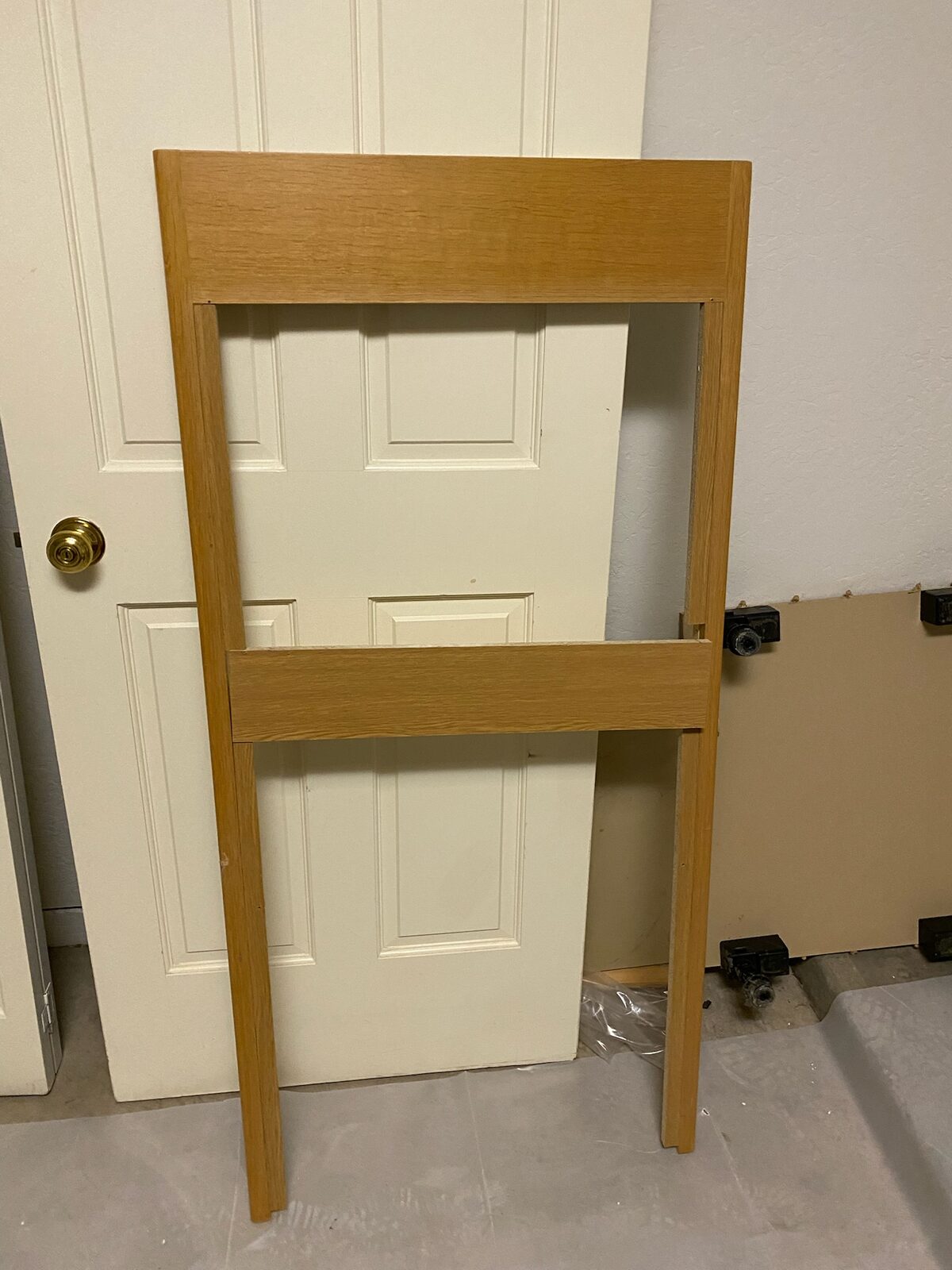 Wood cabinet face frame leaning against a white paneled door during cabinet repair