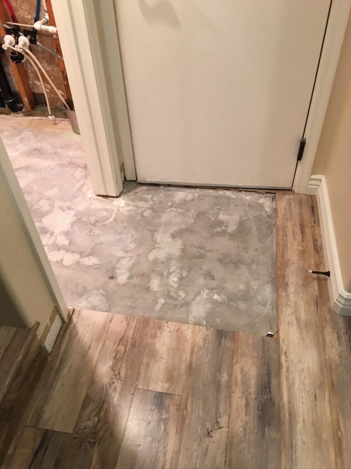 Wood look plank flooring meeting bare concrete at a doorway during a flooring repair