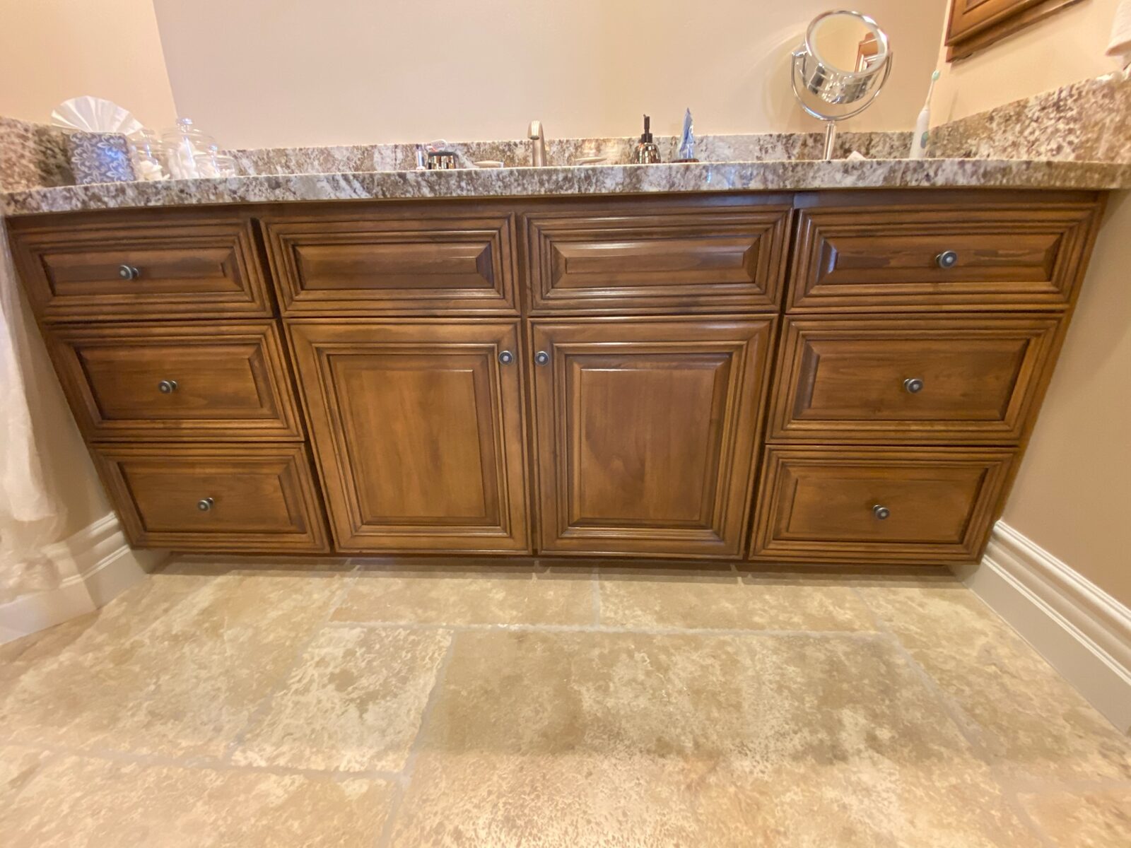 Wood vanity with raised panel doors, granite countertop, and travertine tile floor