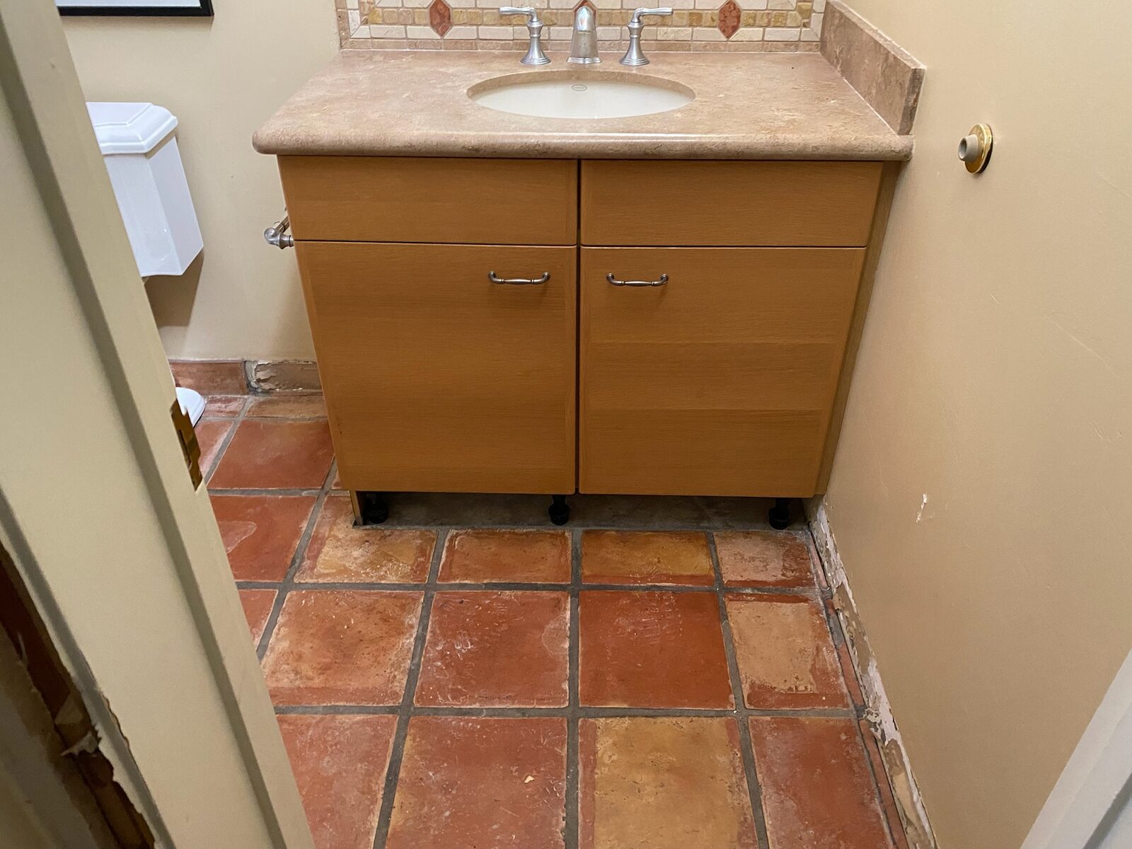 Wood vanity with travertine countertop set on levelers over saltillo tile during a repair
